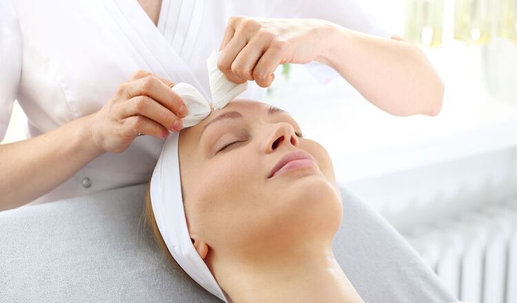 Leżąca kobieta w trakcie zabiegu kosmetycznego na twarzy wykonywanego przez kosmetyczkę